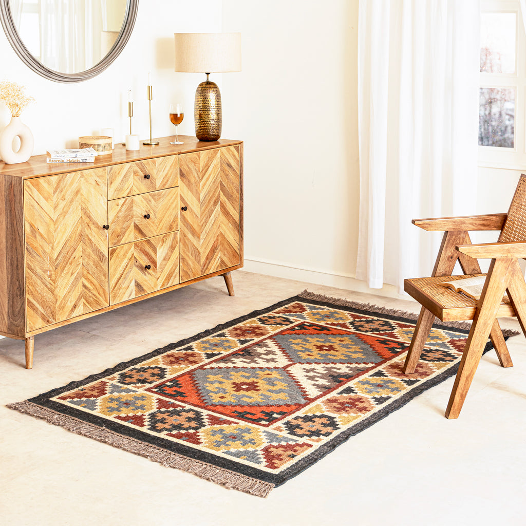 Patterned Kilim Jute rug on a light wood floor with a wooden sideboard and chair in a room.