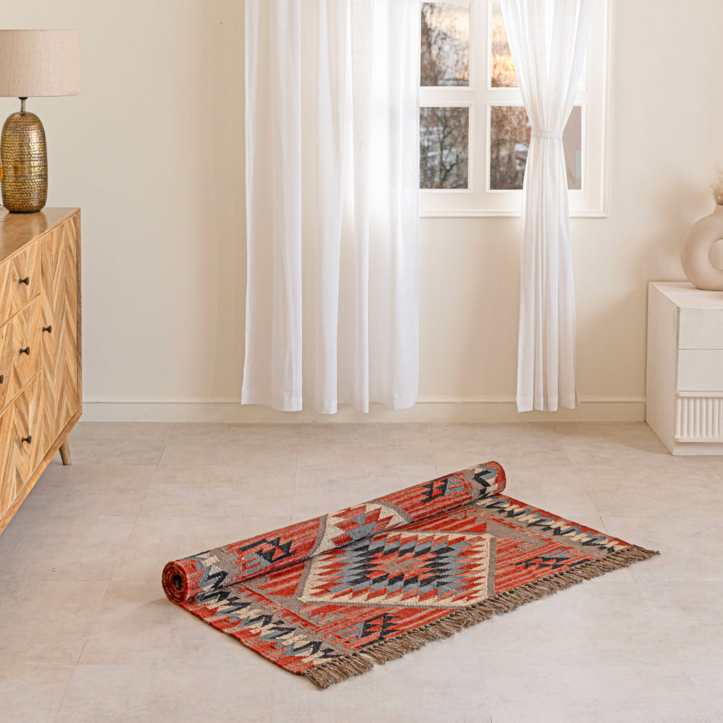 Rolling out a boho kilim rug on a light wooden floor with a sideboard and lamp in the background.