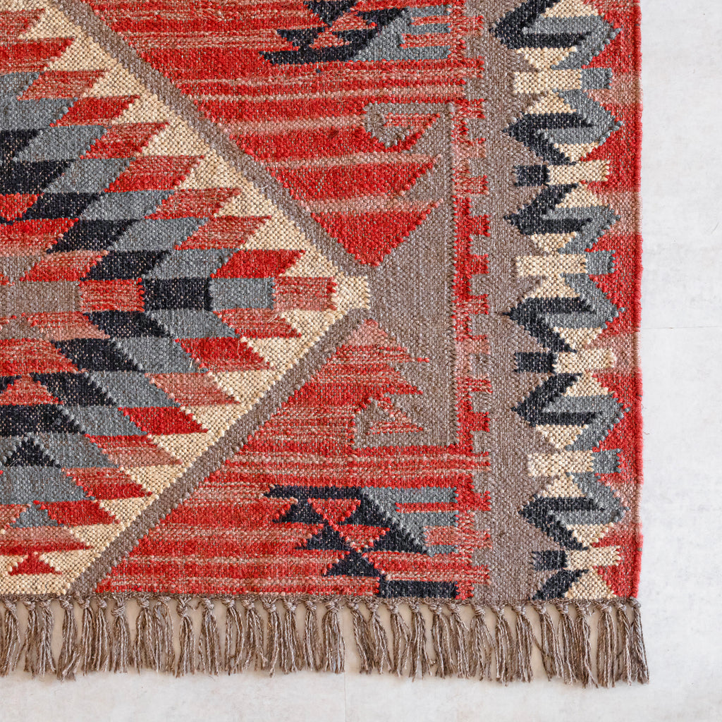 Geometric patterned kilim rug with red, beige, and grey colors on a white background